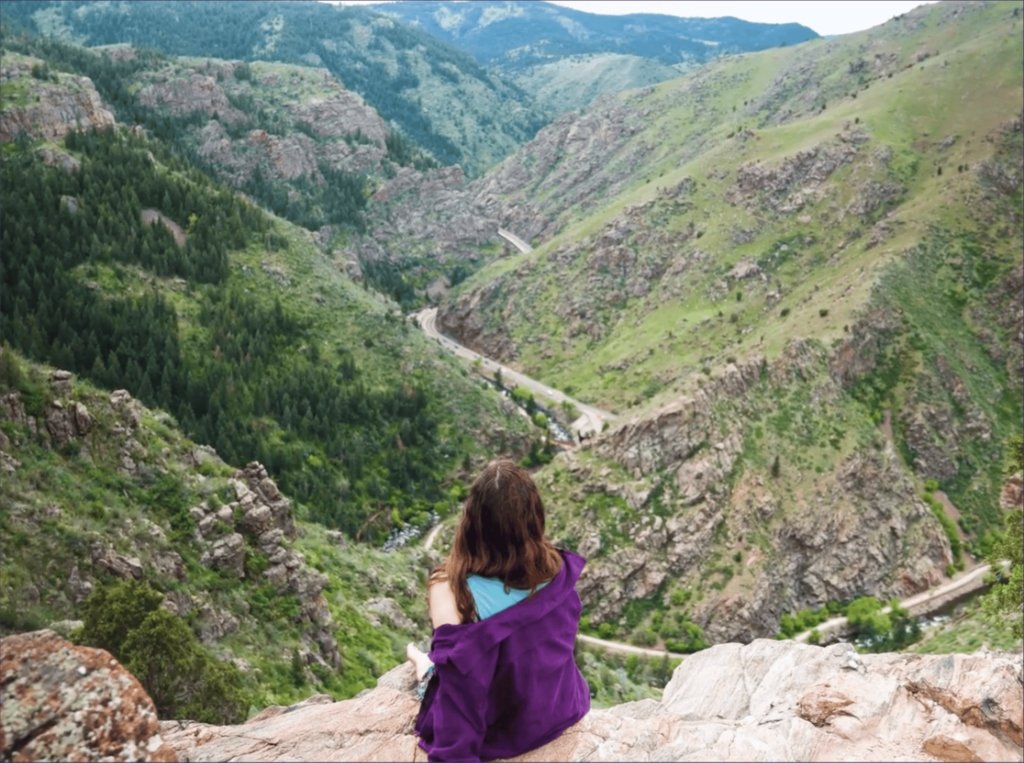 Alex sitting on a cliff looking out at a deep mountain valley